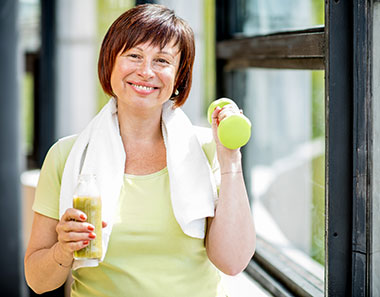 Woman smiling holding healthy juice drink and lifting a weight
